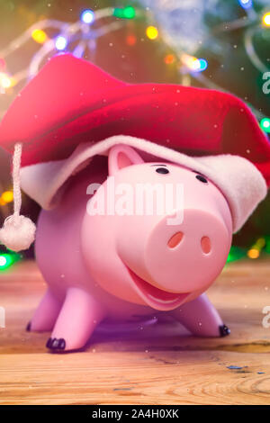 Sparschwein mit Santa Claus Kappe gegen dekoriert Xmas Tree. Christmas Shopping. Geld sparen für Weihnachten. Pre-Christmas ausgaben Konzept Stockfoto