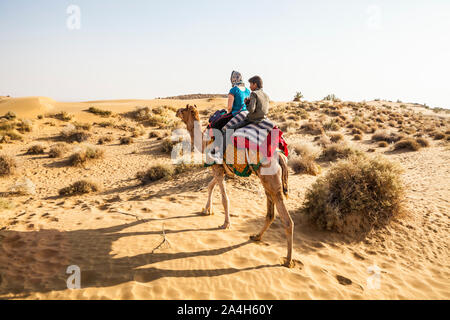 Eine Frau und ihr Kamel guide reiten auf einem Kamel in den Sanddünen von Rajasthan, der Wüste Thar in Indien. Stockfoto