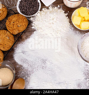 Frisch zubereitete Schokoladenkekse auf einem dunklen Holztisch mit Mehl bestäubt und Zutaten. Stockfoto