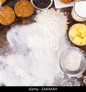 Frisch zubereitete Schokoladenkekse auf einem dunklen Holztisch mit Mehl bestäubt und Zutaten. Stockfoto