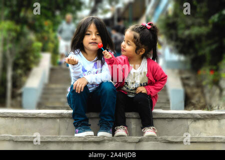 Zwei Mädchen sitzen und essen einen Lutscher im park, sommer Outdoor Portrait. beste Freunde Stockfoto