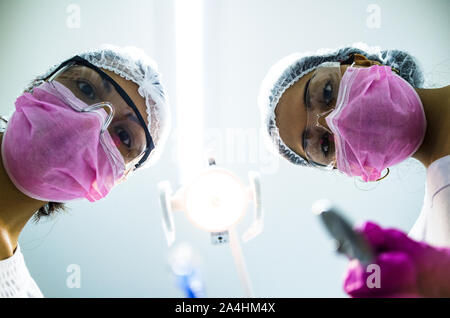 Ansicht von unten zwei Frauen Zahnärzte in chirurgischen Maske Haltewerkzeuge und Kamera. Patient, Zahnarzt. Stockfoto