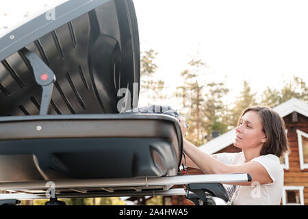 Zufriedene Frau setzt Sachen in der Dachgepäckträger des Autos oder im Ladekasten, vor einer Reise mit der Familie im Urlaub. Close-up. Stockfoto
