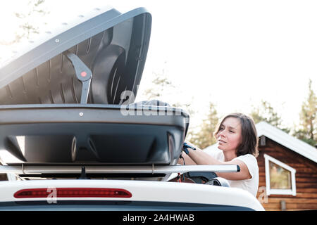 Zufriedene Frau setzt Sachen in der Dachgepäckträger des Autos oder im Ladekasten, vor einer Reise mit der Familie im Urlaub. Close-up. Stockfoto