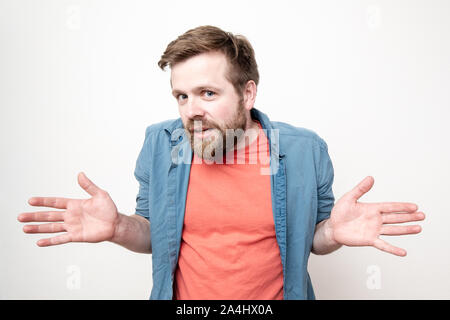 Junge, bärtiger Mann zuckte mit den Schultern, stellt seine Handflächen und sieht in die Kamera mit unschuldigen Augen. Auf weissem Hintergrund. Stockfoto