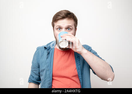 Mann mit einem Papier Becher in der Hand, Getränke und durch ein verdorbenes Getränk ist schockiert, seine Augen weiteten und Horror erscheint auf dem Gesicht. Negative Emotionen. Konzept der verwöhnen Stockfoto