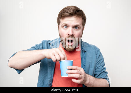 Bärtiger Mann mit einem pappbecher in der Hand, mit Ekel, dauert etwas, aus dem er gerade Kaffee getrunken, mit Blick auf die Kamera mit großen Augen und einem offenen m Stockfoto