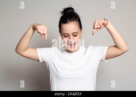 Charmante junge Frau sieht und zeigt mit dem Zeigefinger nach unten, breit grinsend. Auf weissem Hintergrund. Stockfoto