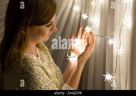 Portrait von eine schöne junge Frau mit braunen Haaren Holding eine beleuchtete sternförmigen Weihnachten Lichterkette in Ihren Händen Stockfoto