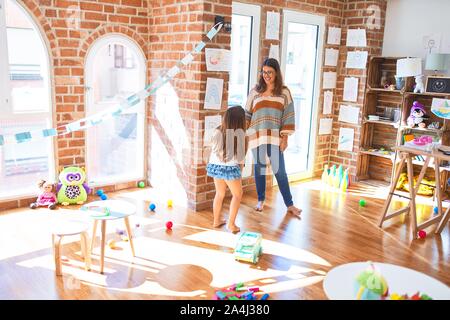 Schöne Lehrer und Kleinkind, lehnt sich an die Wand um viele Spielsachen im Kindergarten Stockfoto