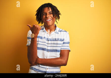 Afro-amerikanische Mann mit Dreadlocks tragen gestreifte Shirt über isolierte gelben Hintergrund lächelnd mit glücklichen Gesicht und mit Verweis auf die Seite Stockfoto