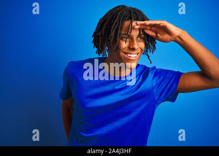 Afro-amerikanische Mann mit Dreadlocks tragende t-shirt stehend über isolierte blauen Hintergrund sehr glücklich und lächelnd weit entfernt, mit der Hand über den Kopf. Stockfoto