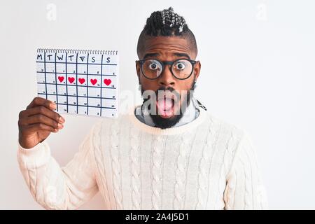 Afrikanische amerikanische Mann mit Zöpfen Haltedauer Kalender über isoliert weißer Hintergrund Angst im Schlag mit einer Überraschung konfrontiert, ängstlich und aufgeregt mit Stockfoto