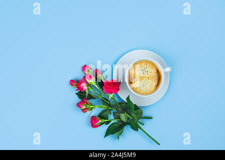 Blauer Hintergrund mit einer Tasse Kaffee von Blumen umgeben. Flach, Ansicht von oben. Stockfoto