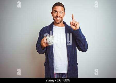 Mann mit bequemen Schlafanzug und Bademantel trinken Tasse Kaffee über isolierte Hintergrund sehr glücklich zeigte mit Hand und Finger Stockfoto