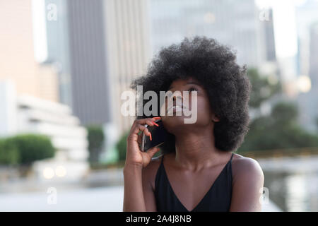 Eine nachdenkliche Afrikanische amerikanische Frau im Gespräch über ein Mobiltelefon, einen Wolkenkratzer auf dem Hintergrund Stockfoto