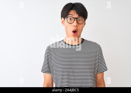 Chinesischer Mann mit Brille und Marine gestreiftes T-Shirt stehend über isoliert weißer Hintergrund Angst und mit Erstaunen Ausdruck, Angst und exc schockiert Stockfoto