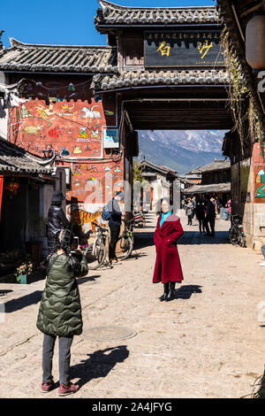 Baisha, China - 11. Februar 2019: Chinesische weibliche Touristen posieren für ein Foto vor dem traditionellen Bai Sha Naxi Dorf Eingangstor in der Nähe von Lijian Stockfoto