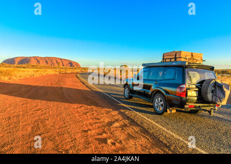 Uluru, Northern Territory, Australien - Aug 25, 2019: 4 x 4-Fahrzeug auf dem Weg zum Ayers Rock, Uluru-Kata Tjuta National Park bei Sonnenuntergang. Majestic Stockfoto