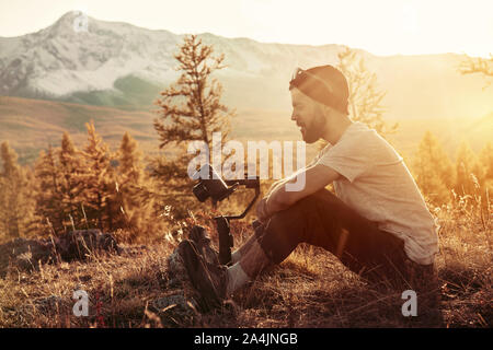 Mann sitzt mit elektronischen Gimbal und DSLR-Kamera gegen Berge Stockfoto
