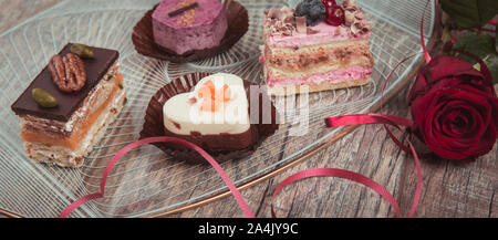 Konzept für ein Café oder eine Bäckerei mit Desserts, festliche Banner. Kleine Kuchen mit verschiedenen Füllungen in der Form eines Herzens Stockfoto