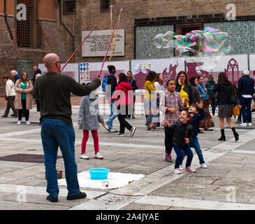 Bologna/Italien - Oktober 12, 2019: Street Performer macht grosse Seifenblasen in Piazza del Nettuno Bologna, Italien. Kinder versammeln sich um ihn glücklich. Stockfoto