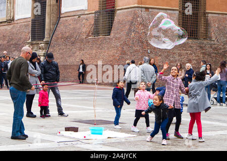 Bologna/Italien - Oktober 12, 2019: Street Performer macht grosse Seifenblasen in Piazza del Nettuno Bologna, Italien. Kinder versammeln sich um ihn glücklich. Stockfoto