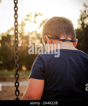 Blonde Junge sieht traurig auf dem Boden auf einem Park Schwingen Stockfoto