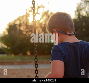 Blonde Junge mit Brille auf den Boden, während auf einer Schaukel sitzend auf einem Spielplatz Stockfoto