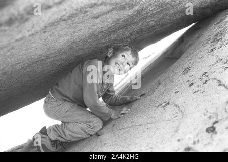 Junge versteckt sich unter rock Stockfoto