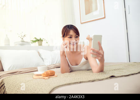 Junge asiatische Frau liegend auf Bett und über Handy in Ihrem Haus zu selfie. Stockfoto