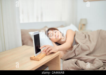 Asiatische Frau schlafend im Bett geweckt durch Alarm am Handy Stockfoto
