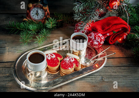 Zwei Tassen Kaffee mit Ingwer Cookies in Form von roten Handschuhe auf Weihnachten ein Stuhl neben den Weihnachtsbaum. Stockfoto