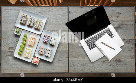 Lieferung einige Teller mit sushis und Notebook auf zwei hölzernen Tisch Stockfoto