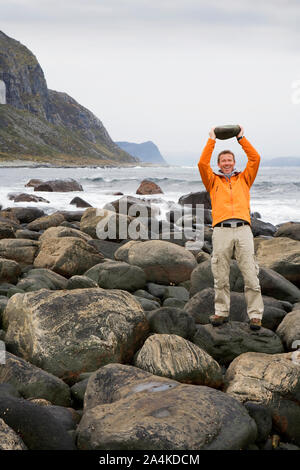 Starke Mann in orange Jacke, Alnes bei Godoy - Anheben von schweren Stein Stockfoto