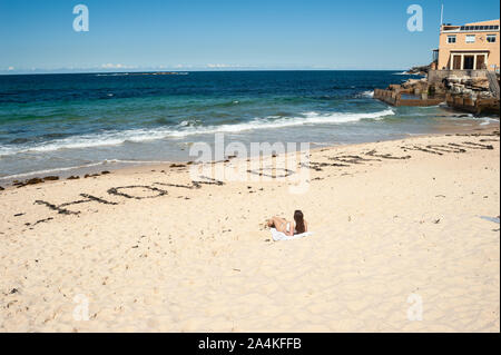 24.09.2019, Sydney, New South Wales, Australien - eine Frau sunbathes in Coogee Beach, wo das Zitat Wie kannst Du es wagen? In den Sand geschrieben. Stockfoto