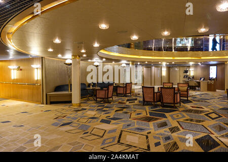 Eine Sitzecke auf einem Kreuzfahrtschiff mit hellgelben Wänden, rot gemusterte komfortable Stühle, gelb gemusterten Teppich und braun Holztischen. Stockfoto