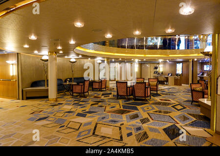 Eine Sitzecke auf einem Kreuzfahrtschiff mit hellgelben Wänden, rot gemusterte komfortable Stühle, gelb gemusterten Teppich und braun Holztischen. Stockfoto