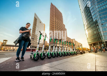 Berlin, Deutschland - Oktober, 2019: Mädchen auf Handy App jetzt von elektrischen E Roller, Escooter oder e-Scooter der Firma Kalk auf Bürgersteig in Berlin Stockfoto