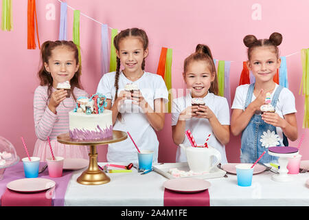 Positive Schöne nette Mädchen holding Cupcakes, Sie Geschmack, lecker Nachtisch. Isolierte rosa Hintergrund, Studio shot Stockfoto