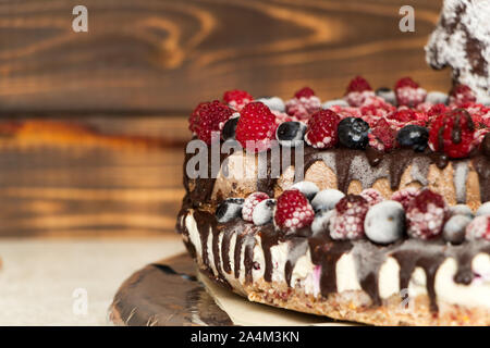Eine Nahaufnahme eines Vegane Schokoladentorte mit Himbeeren und Blaubeeren bedeckt, in den Kühlschrank eingefroren, auf einem Tisch mit verschwommenen Hintergrund. Kopieren Stockfoto