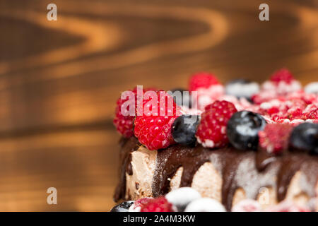 Eine Nahaufnahme eines Vegane Schokoladentorte mit Himbeeren und Blaubeeren bedeckt, in den Kühlschrank eingefroren, auf einem Tisch mit verschwommenen Hintergrund. Kopieren Stockfoto