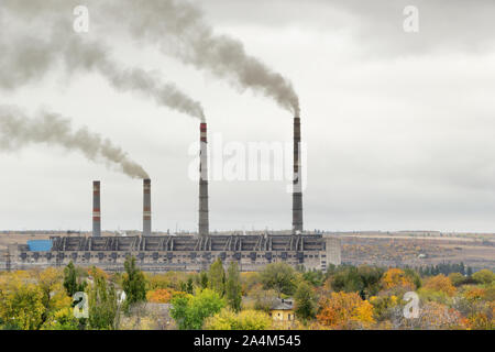 Luftverschmutzung Konzept. Thermische Kraftwerk Gebäude mit Schornsteinen mit Wolken von Rauch gegen grauen Herbsthimmel. Grün, gelb, orange Bäume in Stockfoto