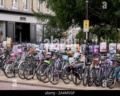 Cambridge, UK - Oktober 9, 2019: Fahrräder gegen den Zaun mit einer Menge Poster geparkt. Stockfoto