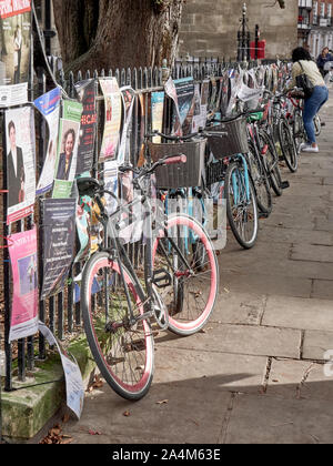 Cambridge, UK - Oktober 9, 2019: Fahrräder gegen den Zaun mit einer Menge Poster geparkt. Stockfoto