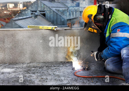 Mann in Sicherheit Ausrüstung Schweißen auf dem Dach Stockfoto