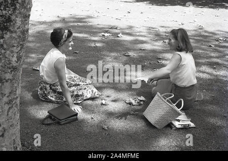 1960er Jahre, historische und sommerliche Studenten und zwei Studentinnen sitzen auf dem Gras und plaudern miteinander auf dem Gelände der University of Southern California (USC) in Los Angeles, USA. Stockfoto