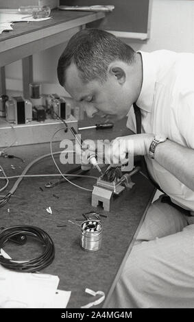 1960er Jahre, historisch, ein erwachsener Student, der in einer Werkstatt arbeitet, mit einem Lötkolben an einem elektrischen Sicherungskasten, USA. Stockfoto