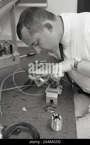 1960er Jahre, historisch, ein erwachsener Student, der in einer Werkstatt arbeitet, mit einem Lötkolben an einem elektrischen Sicherungskasten, USA. Stockfoto