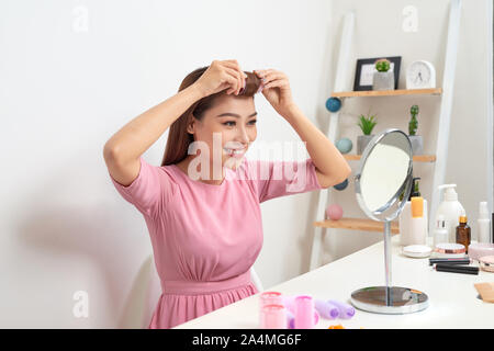 Kopf und Schultern Portrait von schöne asiatische Frau Haar Lockenwickler in Spiegel mit breitem Lächeln suchen, Home Interior auf Hintergrund Stockfoto